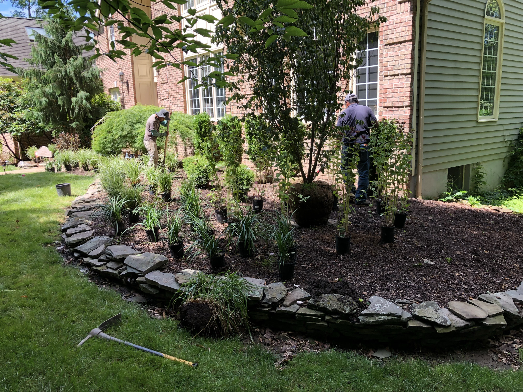 Crew installing shrubs and perennials in a stone-edged garden bed in Glenside, PA