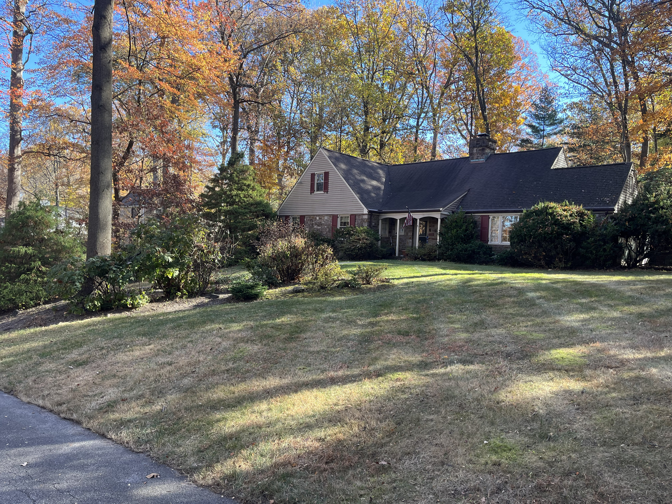 Healthy green front lawn and tidied beds at the same stone home after lawn care in Montgomery County, PA